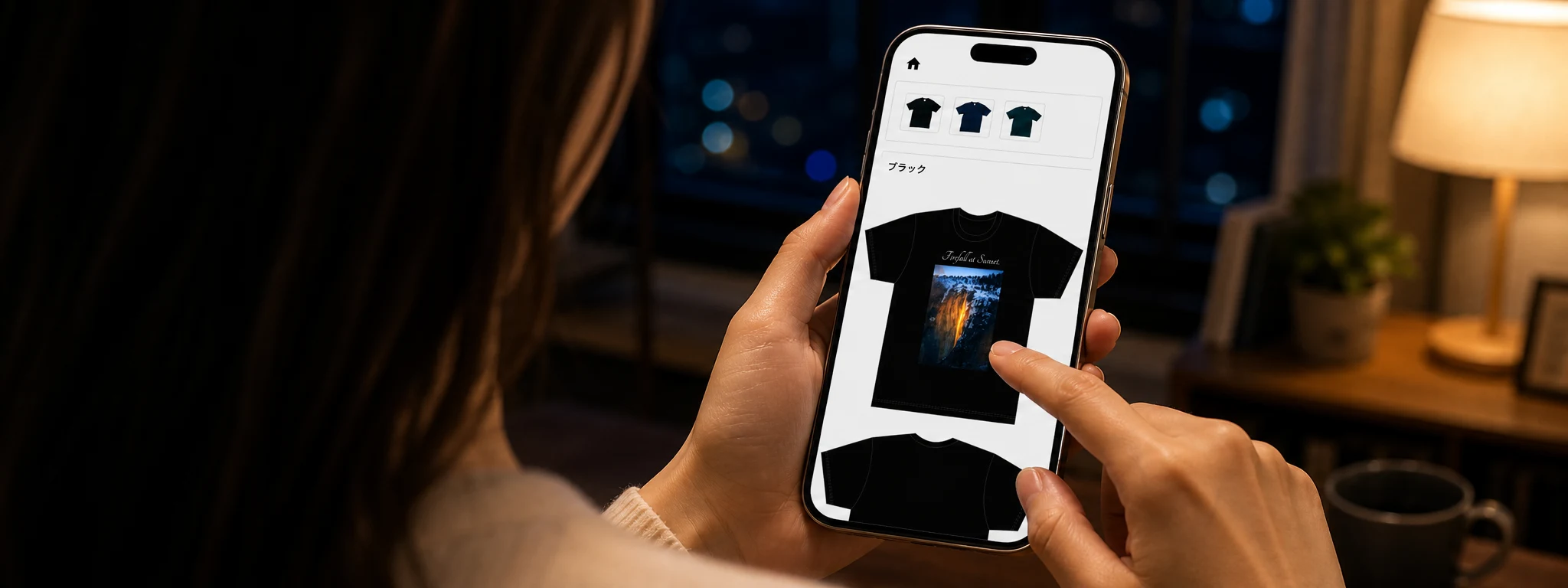 夜の落ち着いた室内で、iPhone 17 Proを使ってオリジナルTシャツのデザインを作成する手元